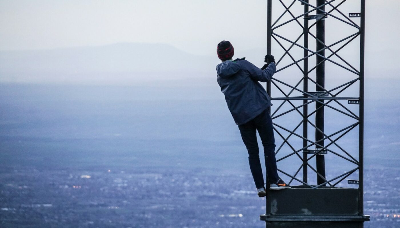 man climbing on tower near buildings at daytime